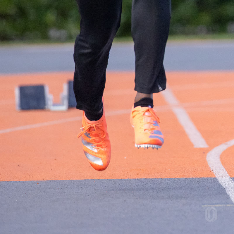 Close-up of an elite sprinter's foot and ankle in dorsiflexion, with toes pulled up toward the shin just before striking the track, a key technique in tendon training