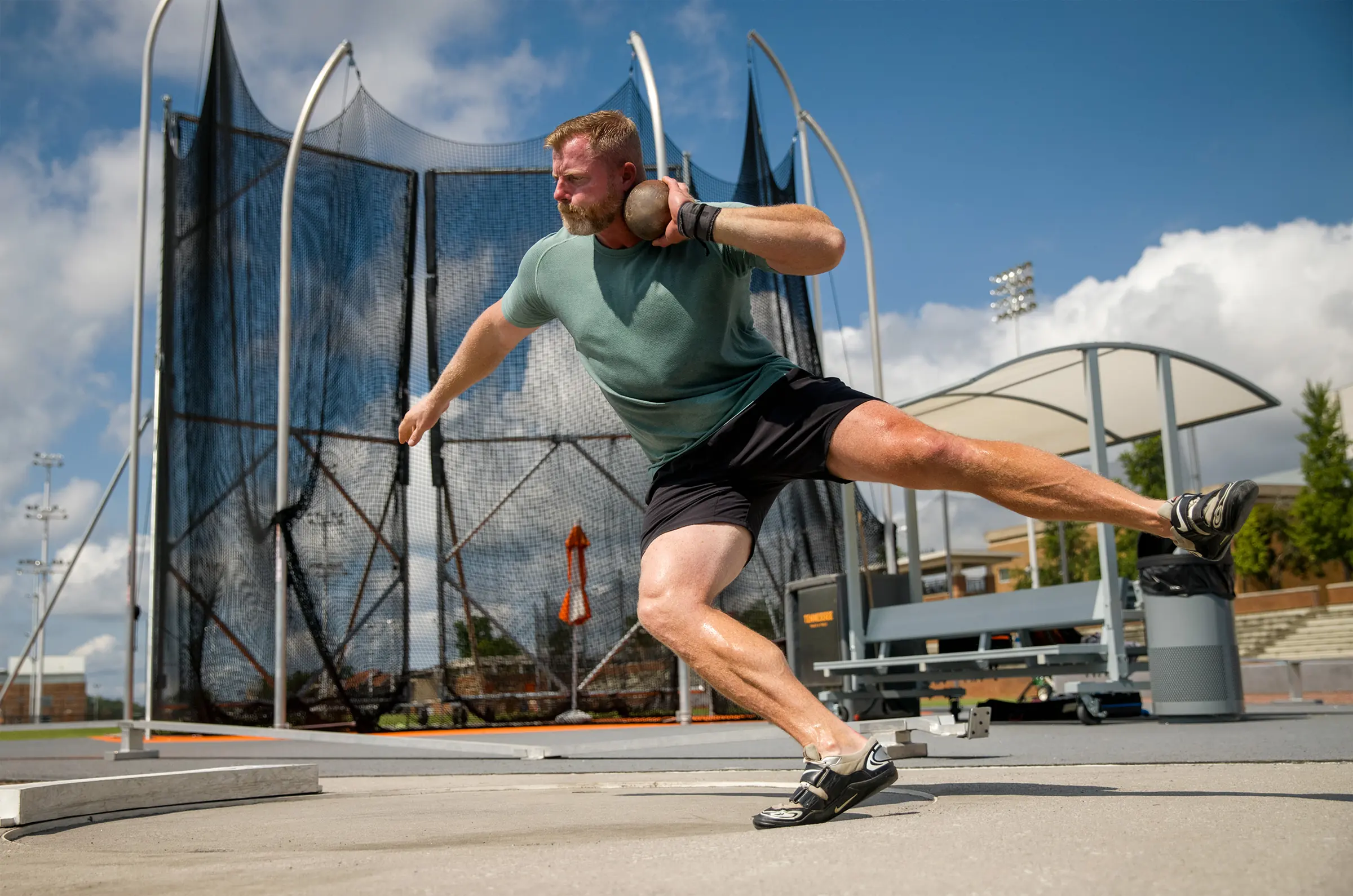 A shot putter driving through the throw in front of the cage